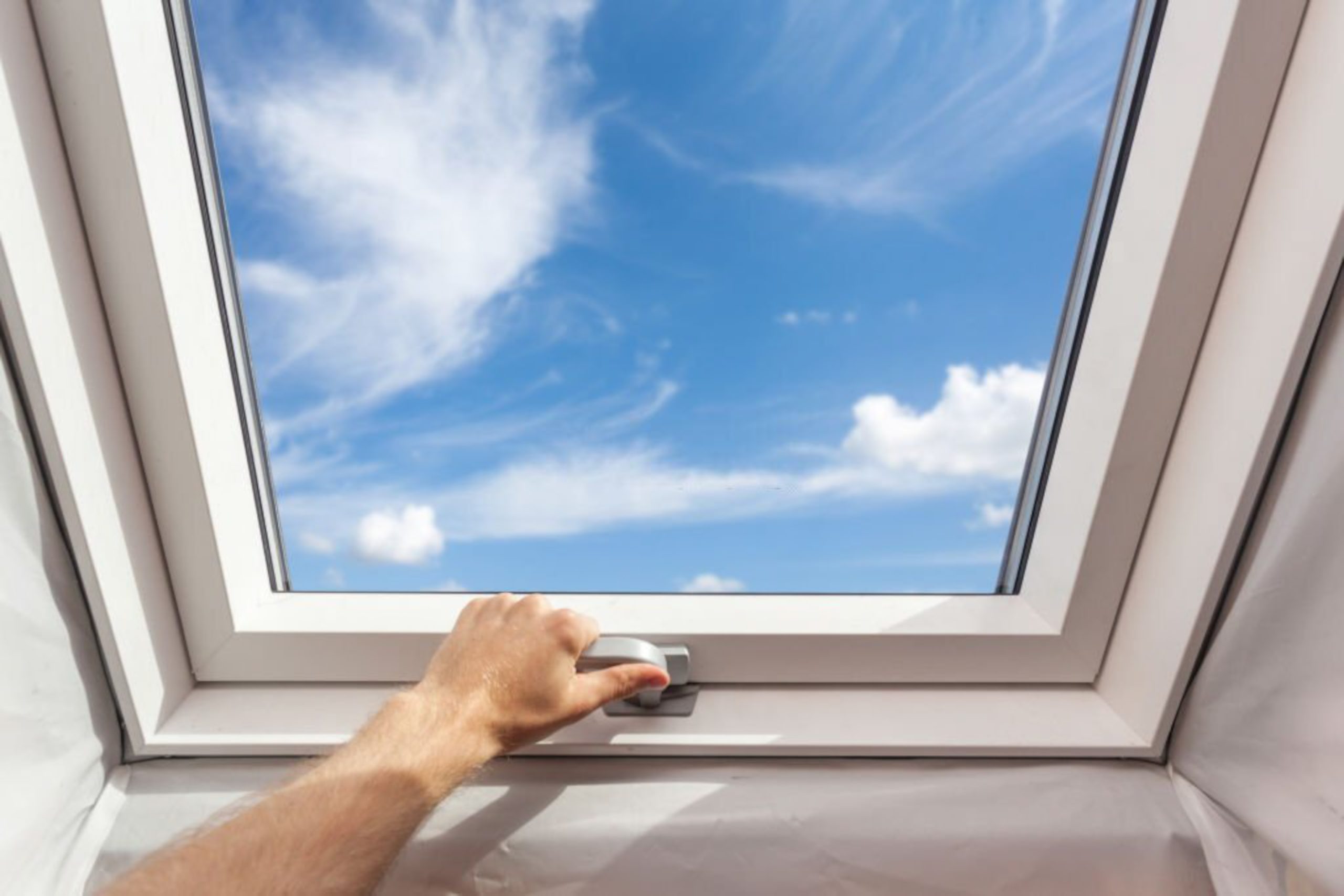 Man close new skylight (mansard window) in an attic room against blue sky